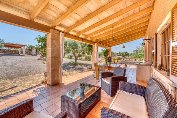 Une terrasse extérieure aménagée avec des meubles en osier, une table à plateau de verre et une vue sur le paysage environnant.