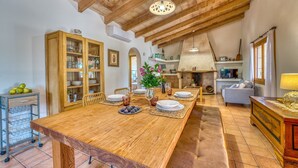 Ein geräumiger Essbereich mit einem langen Holztisch, eine Küche mit Kamin aus Stein und eine gemütliche Sitzecke mit Sofa und Sessel.
