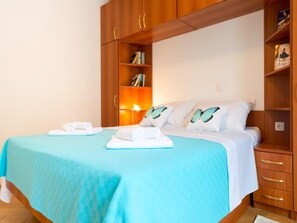 A hotel room with a bed, a nightstand, a wooden wardrobe, and a shelf with books.