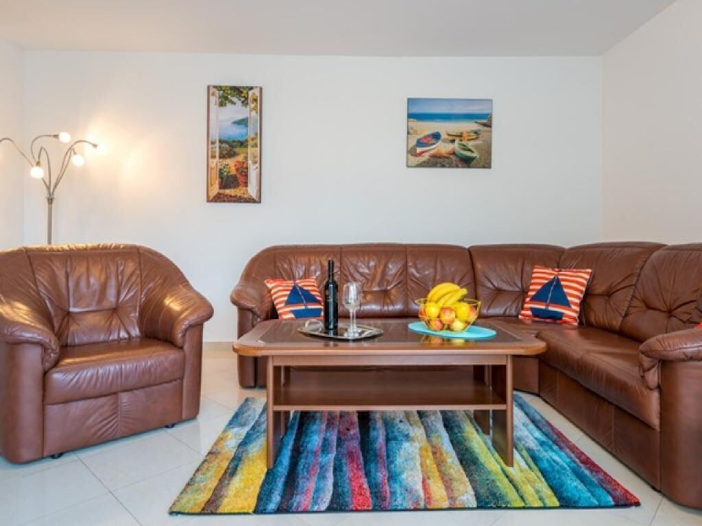 A living room with a brown leather sofa, a coffee table with fruit and a bottle, and two wall-mounted paintings.