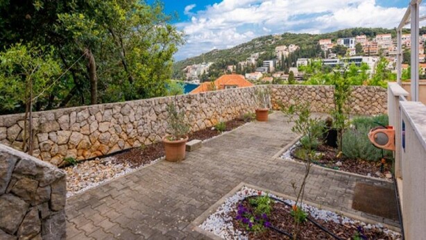 A stone wall, potted plants, and a paved patio with a view of a hillside town. - Feel Good Apartment (Dubrovnik)