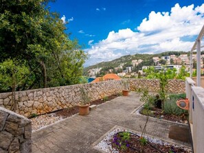 A stone wall, potted plants, and a paved patio with a view of a hillside town. - Feel Good Apartment (Dubrovnik)