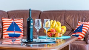 A wooden table with a bottle of wine, two glasses, and a fruit basket on a blue coaster. - Feel Good Apartment (Dubrovnik)