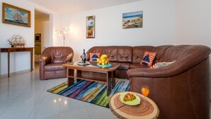 A living room with a brown leather sofa, a coffee table with fruits and a drink, a small round table with a croissant, and a colorful striped rug. - Feel Good Apartment (Dubrovnik)