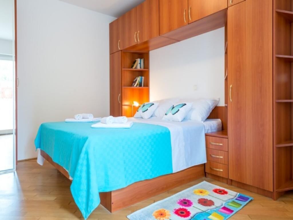 A bedroom with a bed, wooden wardrobe, and a small shelf with books.