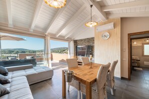 Amplia sala de estar con una mesa de comedor de madera, sillas de mimbre, un sofá y vistas al exterior.