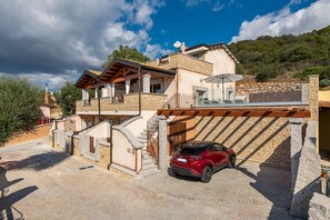 A multi-story house with a car parked in the driveway, stone walls, and a balcony.