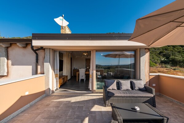 A balcony with a wicker sofa, a table, and a glass door leading to an indoor area.