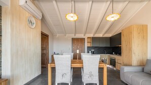 Ein Essbereich mit Holztisch und Korbstühlen, eine Küche mit dunklen Schränken und ein graues Sofa.
