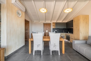 A dining area with a wooden table and wicker chairs, a kitchen with dark cabinets, and a gray sofa.