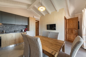 A modern kitchen with grey cabinets, a wooden dining table, wicker chairs, and a TV mounted on the wall.