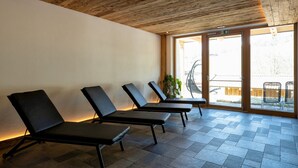 A room with three black lounge chairs, wooden ceiling, and large windows with a view of the outside.