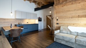 A modern kitchen with wooden beams, a dining area with a table and chairs, and a living area with a sofa and a unique tree sculpture.