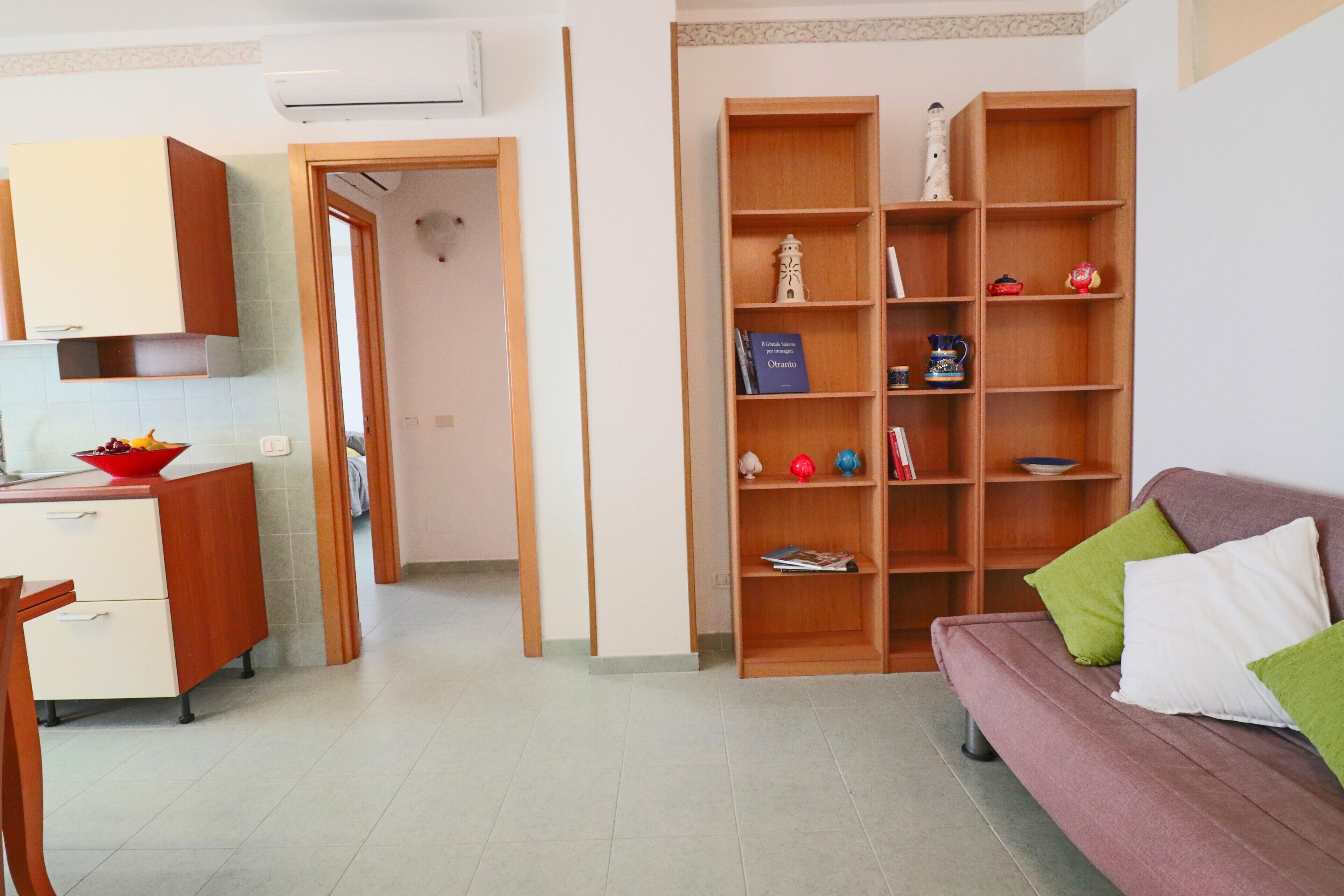 A living room with a sofa, a bookshelf, and a kitchen area with cabinets and a countertop.
