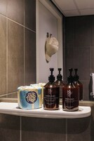 A bathroom with a shelf holding toiletries, a towel rack, and a wall-mounted towel rack.