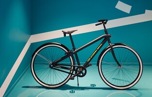A bicycle with a black frame and yellow accents, positioned against a blue wall with white geometric shapes.