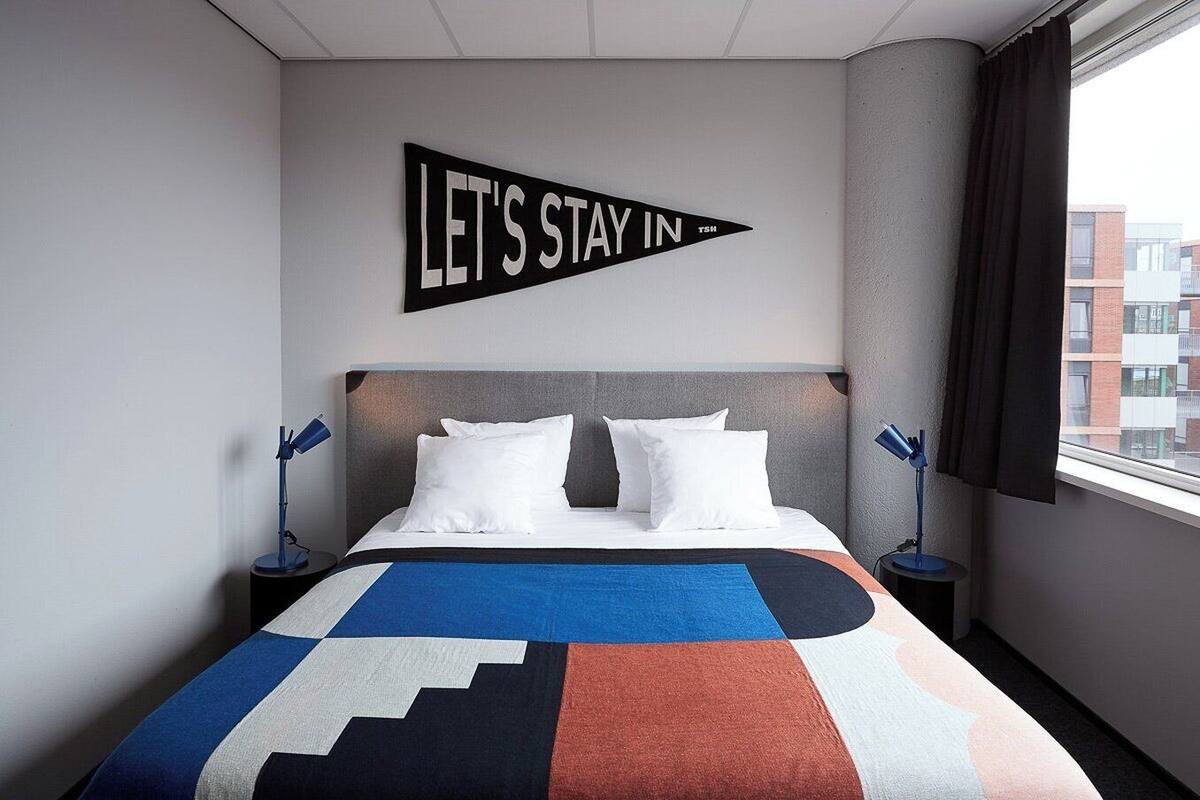 Een moderne hotelkamer met een groot bed, twee nachtkastjes, een hoofdbord en een raam met gordijnen.