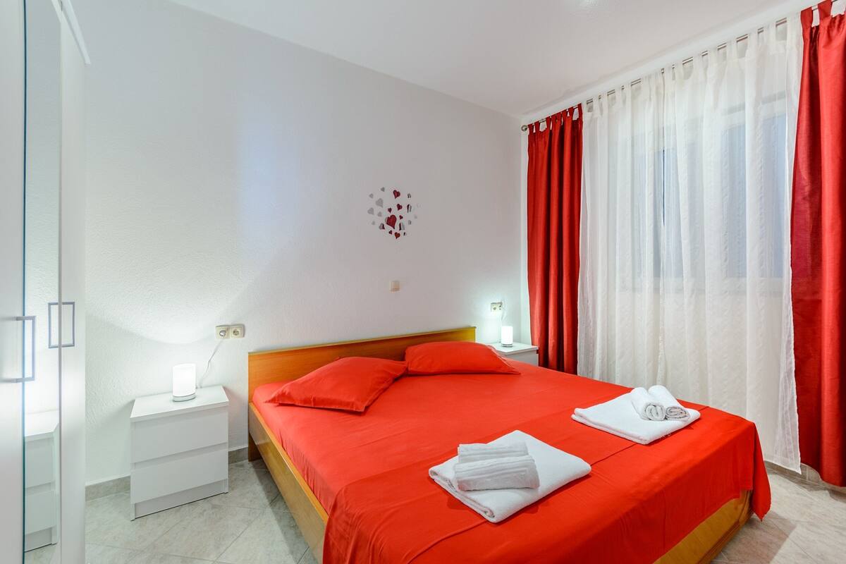Une chambre d’hôtel avec un lit, une table de chevet, une lampe et une fenêtre avec des rideaux.