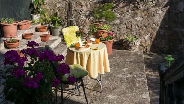 A stone patio with a round table and a chair, surrounded by potted plants and flowers. - Apartment Jeanny (Dubrovnik)
