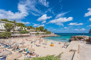 Une plage avec des parasols, des gens qui prennent des bains de soleil et une côte rocheuse.