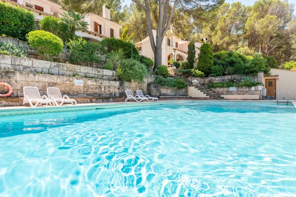 Une piscine avec des chaises longues, un mur en pierre et un bâtiment doté de balcons en arrière-plan.