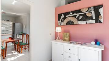 A dining area with a wooden table and chairs, a white cabinet with drawers, and a pink wall with a black and white artwork.