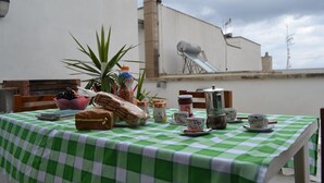 A table with a green and white checkered tablecloth, a coffee pot, cups, a jar of jam, a bowl of fruit, and a plant.