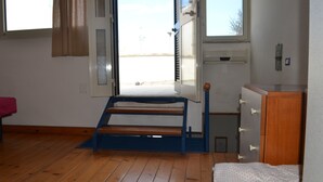 A room with a bed, a window, a wooden floor, a door, and a small cabinet.