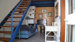 A living room with a blue staircase, a sofa, a television, and a white wicker table.