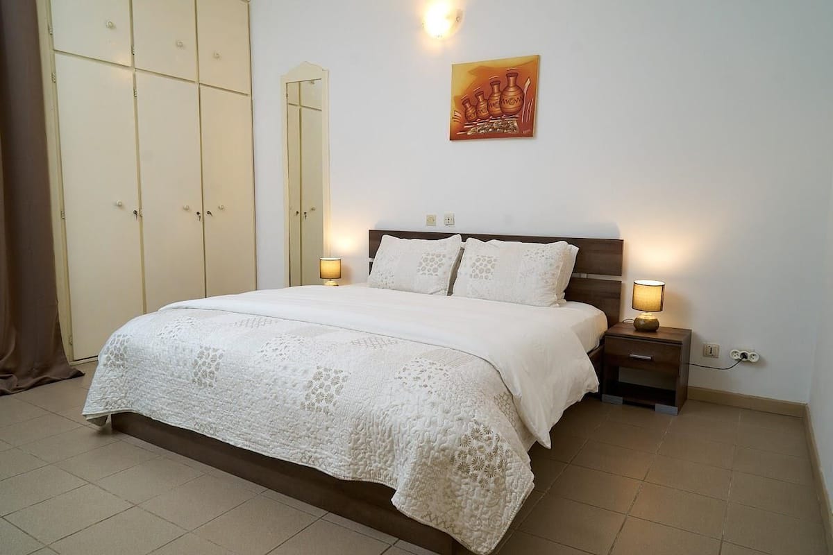 A bedroom with a large bed, two bedside lamps, a nightstand, and a wardrobe.