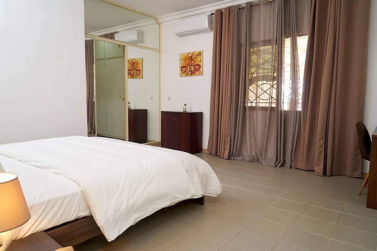 A bedroom with a bed, a dresser, a mirror, and a window with curtains.