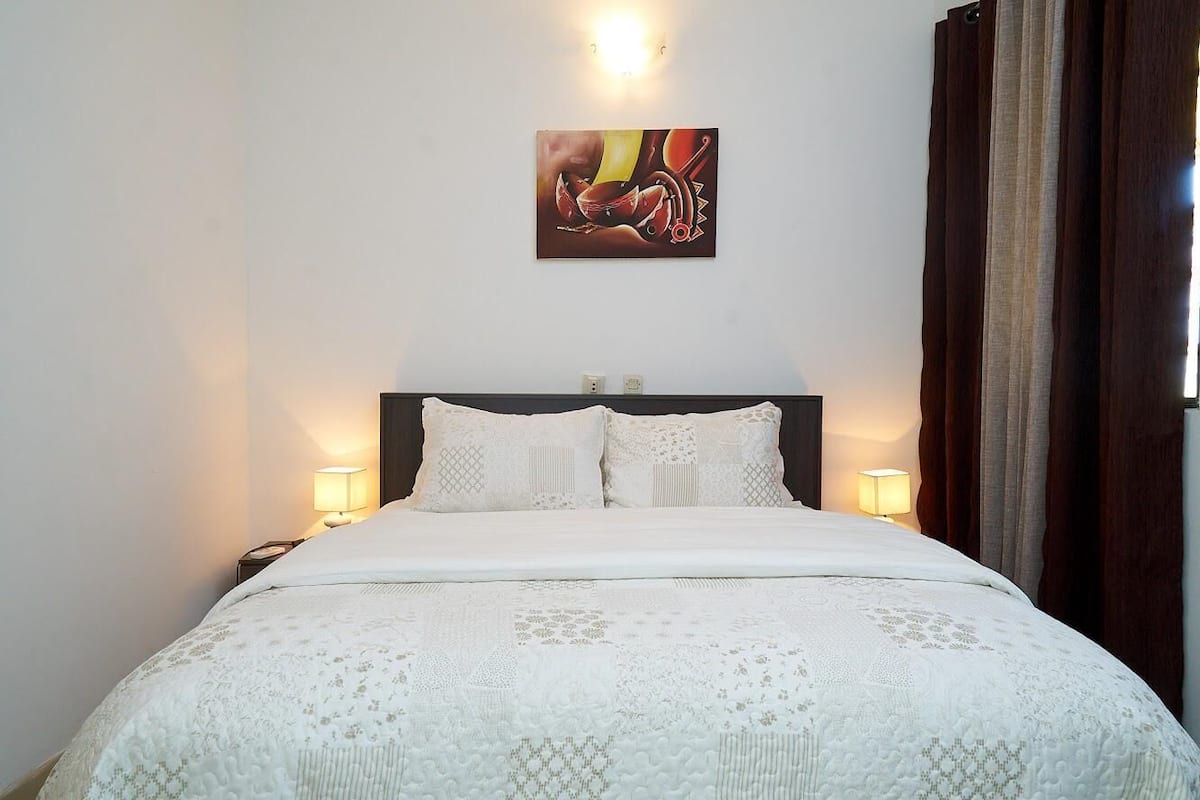 A neatly made bed with a white comforter and pillows, a dark headboard, and a painting above it.