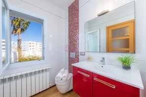 A modern bathroom with a large window, a white toilet, a red cabinet, and a mirror with a wooden frame.