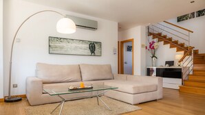 A modern living room with a beige sofa, a glass coffee table, a floor lamp, and a staircase leading to an upper level. - Fantastic Villa with Pool, Rooftop Terrace, Air Conditioning, and Wi-Fi (Cala d'Or)