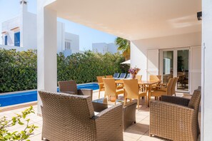 An outdoor patio with wicker furniture, a pool, and a view of a white building with blue shutters.