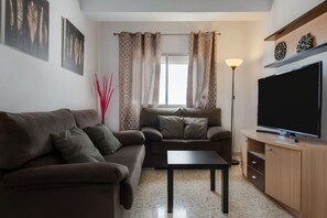 A living room with a sofa, a coffee table, a TV on a wooden cabinet, and a floor lamp.