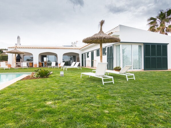 A modern villa with a swimming pool, outdoor seating, and a thatched roof structure.