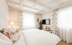 Une chambre à coucher avec un grand lit, un téléviseur fixé au mur et une plante.