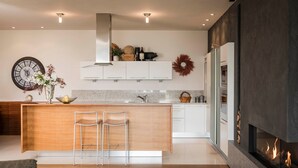 Une cuisine moderne dotée d’un îlot central, de tabourets de bar, d’une horloge et d’une cheminée.