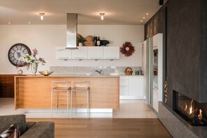 A modern kitchen with a central island, bar stools, a clock, and a fireplace.