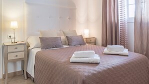 Un lit bien fait, recouvert d’une couverture marron, deux tables de chevet avec des lampes et une fenêtre avec des rideaux.