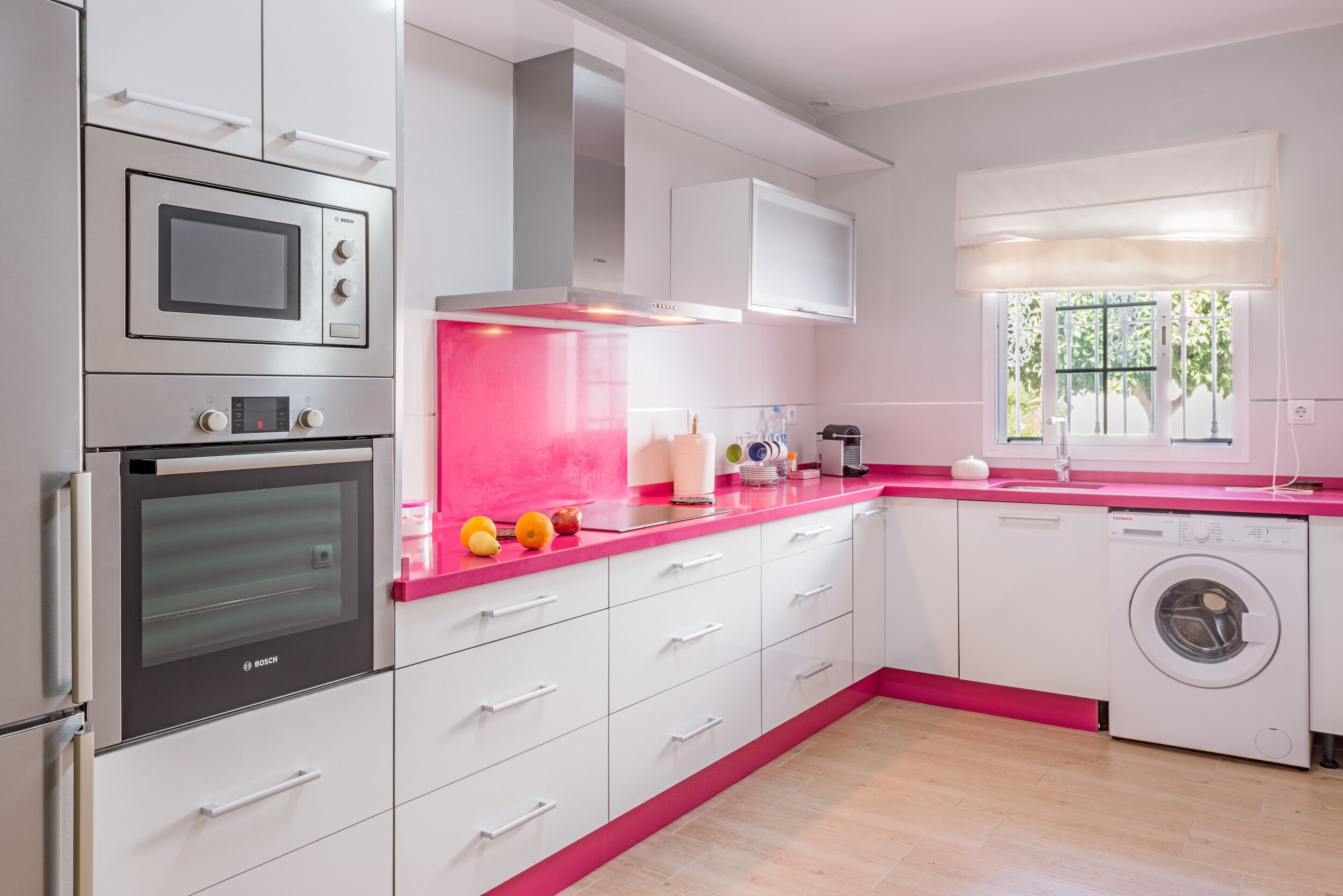 A modern kitchen with white cabinets, a Bosch oven, a washing machine, and a pink countertop.