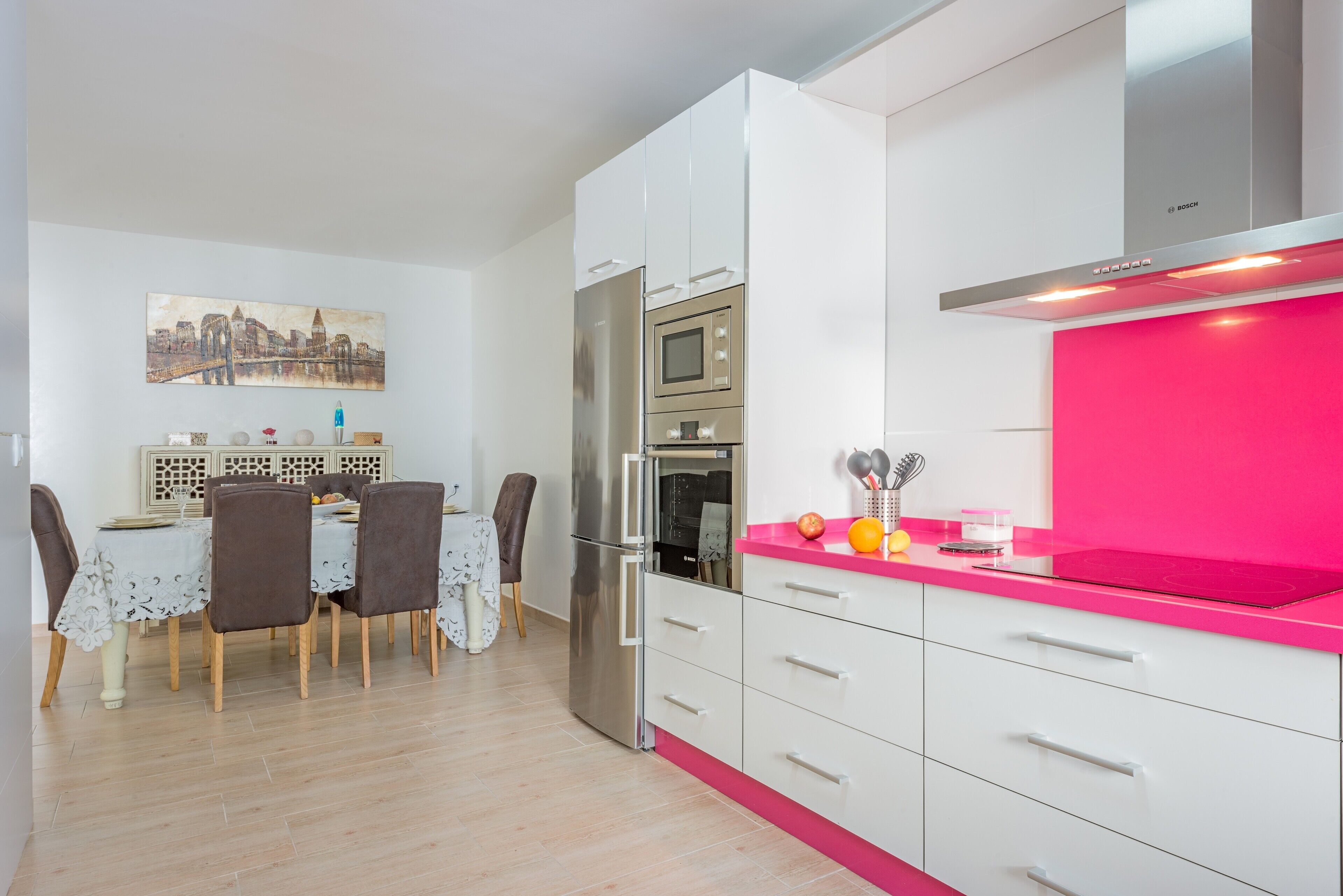 Eine moderne Küche mit weißen Schränken, einer pinkfarbenen Arbeitsplatte und einem Essbereich mit Tisch und Stühlen.