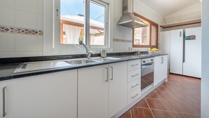 A kitchen with white cabinets, a black countertop, a stainless steel sink, a built-in oven, and a window with blinds. - Beautiful Country House with Pool, Terraces & Wi-Fi; Parking Available (Artá)
