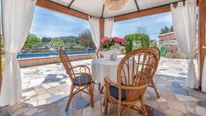 A covered outdoor seating area with wicker chairs and a table, overlooking a pool and greenery. - Beautiful Country House with Pool, Terraces & Wi-Fi; Parking Available (Artá)