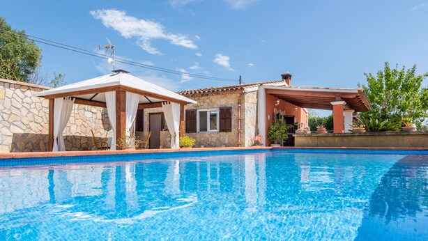 A swimming pool with a stone wall and a covered area. - Beautiful Country House with Pool, Terraces & Wi-Fi; Parking Available (Artá)