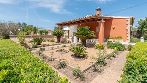 A building with a red facade, a tiled roof, and a garden with various plants and a pathway. - Beautiful Country House with Pool, Terraces & Wi-Fi; Parking Available (Artá)