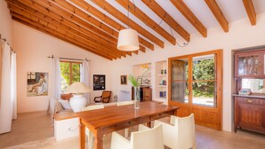 A dining area with a wooden table and chairs, a hanging light fixture, and a view through a glass door. - Beautiful Finca with Wi-Fi, Pool, Lawn, and Patio; Parking Available (Son Servera)