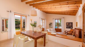 A spacious room with a wooden ceiling, a dining table with chairs, a sofa, and a view of the outdoors. - Beautiful Finca with Wi-Fi, Pool, Lawn, and Patio; Parking Available (Son Servera)