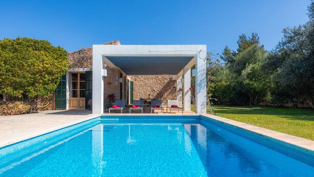 A swimming pool with a covered seating area, a stone wall, and greenery. - Beautiful Finca with Wi-Fi, Pool, Lawn, and Patio; Parking Available (Son Servera)